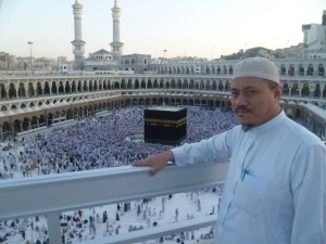 Dato’ Dr. Abu Anas Madani berdiri di tingkat atas Masjidil Haram dengan Kaabah dan jemaah tawaf di belakang